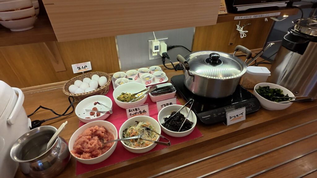 朝食バイキングのメニュー(ご飯、生卵、納豆、梅干し、高菜漬け、のり、明太子、春雨、ごま昆布、コーンスープ、味噌汁)